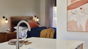 Habitación de hotel con una cama, lámparas de noche, una mesita de noche, un vaso de agua y un cuadro en la pared.
