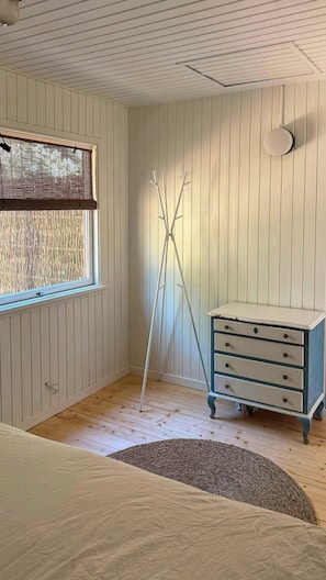Ein Zimmer mit einem Bett, einem Schminktisch, einem Fenster mit Jalousien, einem Stativ und einem Deckenventilator.