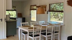 Huone, jossa on ruokapöytä, tuoleja, sohva, pieni keittiö ja ikkuna, josta on näkymä vehreään maisemaan.