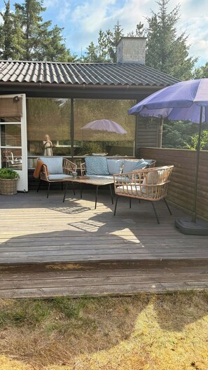 Eine Terrasse im Freien mit Korbmöbeln, einem überdachten Sitzbereich und einem Holzboden.