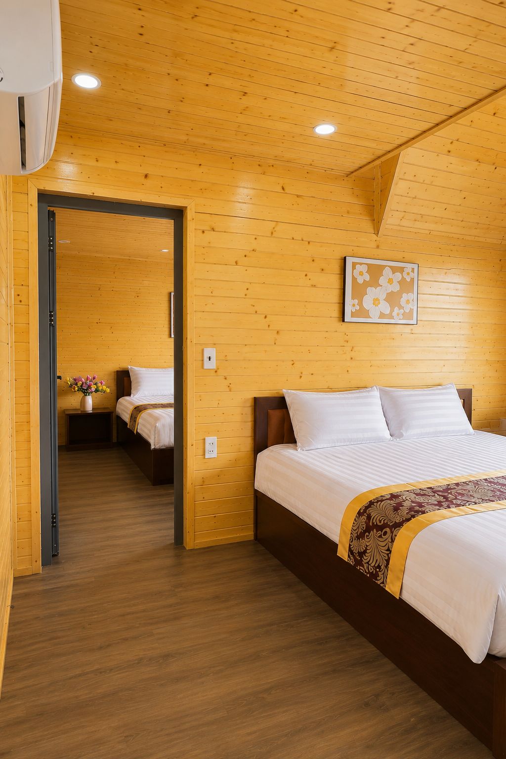 Ein Zimmer mit Holzwänden, einem Bett, einem Nachttisch mit Blumen und einem an der Wand hängenden Bild.