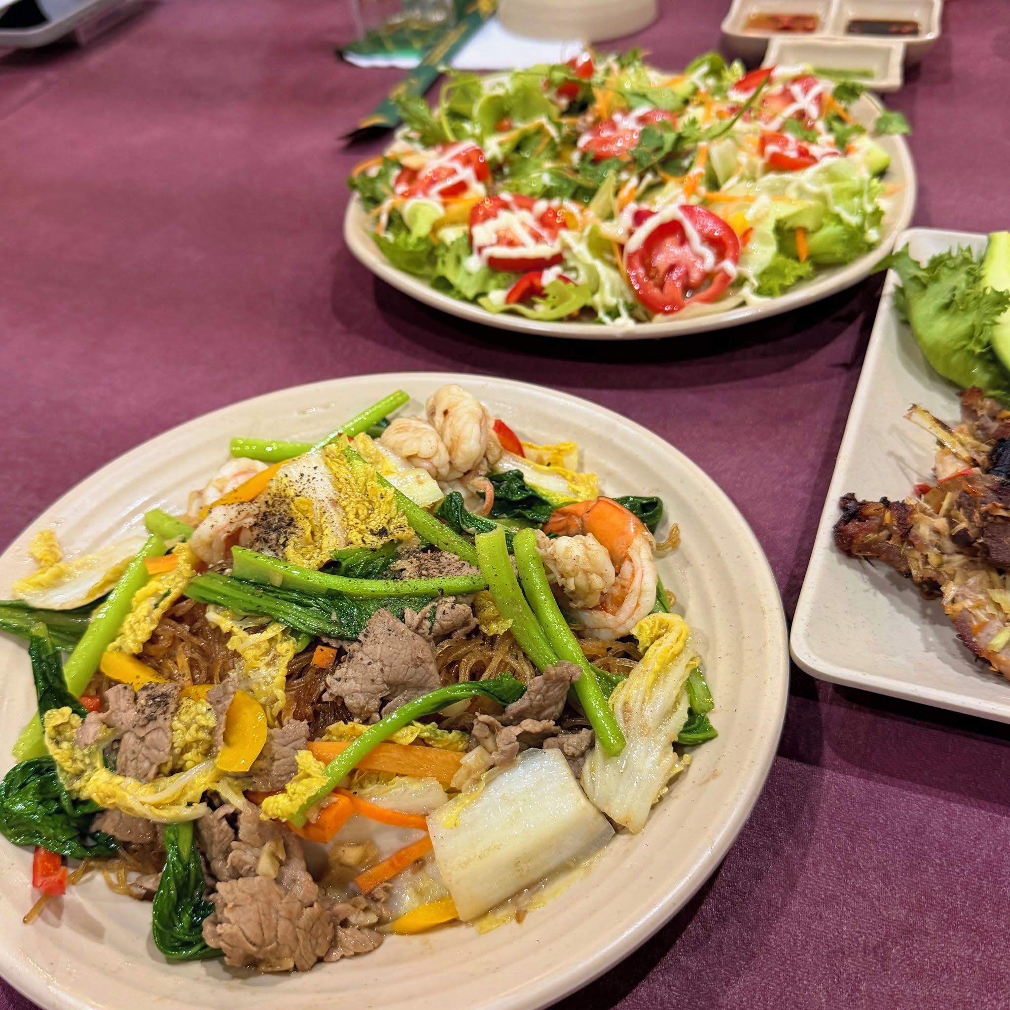 A table with various dishes, including a plate of stir-fried vegetables and meat, a salad, and a dish with grilled meat.