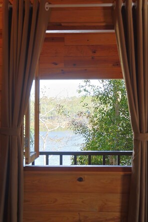 A wooden cabin with a window featuring a view of a lake and trees.