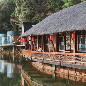 A traditional wooden structure with a thatched roof, overwater walkway, and red lanterns.