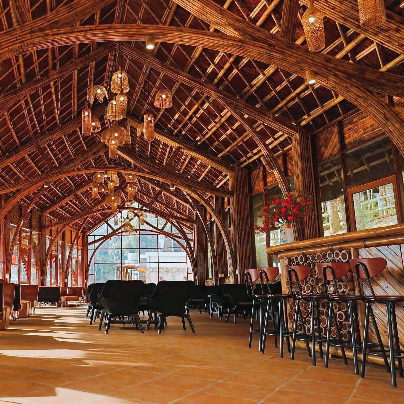 Un interior con un techo de madera alto y arqueado, lámparas de mimbre colgantes y una zona de bar con taburetes.