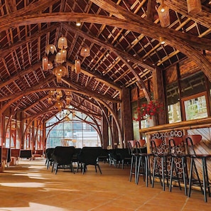 An interior with a high, arched wooden ceiling, hanging wicker lamps, and a bar area with stools.