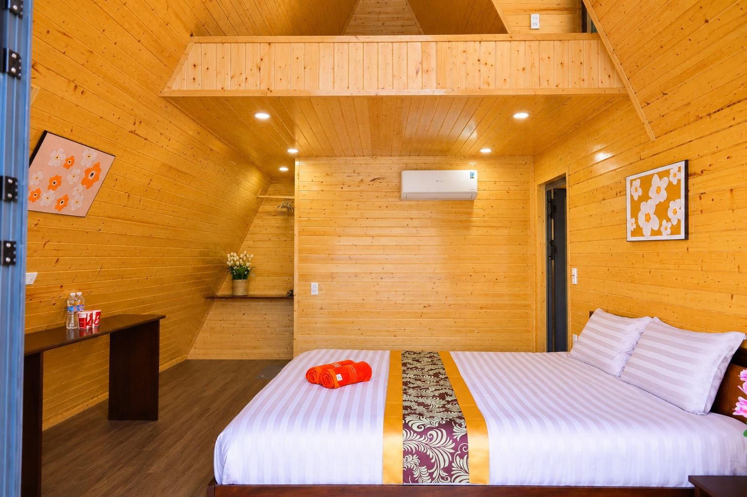Ein Zimmer mit Holzwandverkleidung, einem Bett, einem kleinen Tisch mit einer Wasserflasche und einer Wand-Klimaanlage.