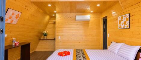 A wooden-paneled room with a bed, a small table with a water bottle, and a wall-mounted air conditioner.