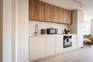 Una cocina moderna con armarios blancos, un estante superior de madera, un microondas, un hervidor y una estufa.