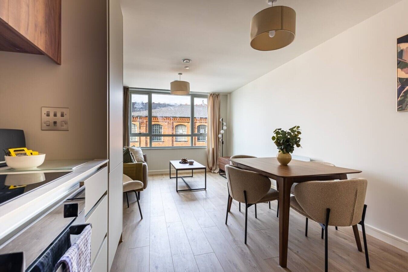 A modern kitchen with a dining area, a view of a brick building, and a large window.