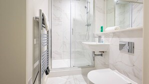 Moderni kylpyhuone, jossa on lasiseinällä varustettu suihku, valkoinen pesuallas ja wc.