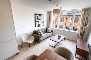 Uma sala de estar moderna com sofá, cadeiras, mesa de centro e vista para um edifício de tijolos através de uma janela grande.