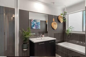 A modern bathroom with a large mirror, a sink, and a bathtub.