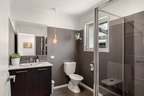 A modern bathroom with a glass shower enclosure, a white toilet, and a dark-colored vanity.