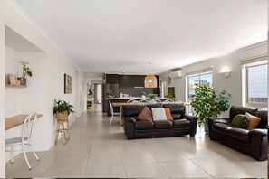 Uma sala de estar moderna com sofá, mesa de jantar e cadeiras. Uma cozinha visível ao fundo.