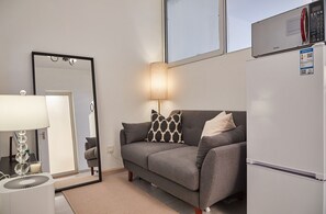 A modern living room with a grey sofa, a large mirror, a standing lamp, a white refrigerator, and a window above the sofa. - Innocondo Extended Stay Jing'an Yuyuan Road (Shanghai)