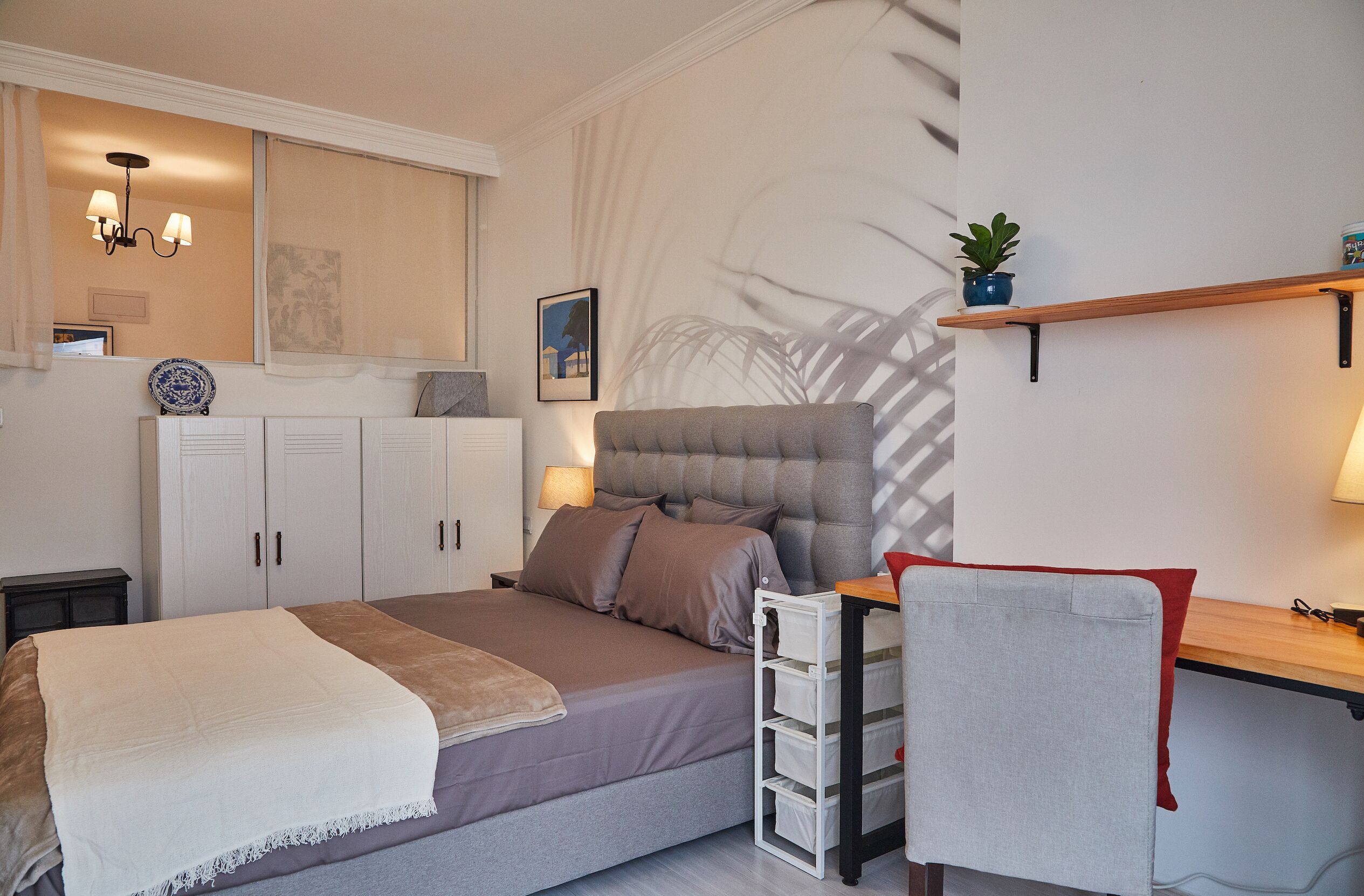 Un dormitorio con cama, mesitas de noche, un escritorio y una estantería con una planta.