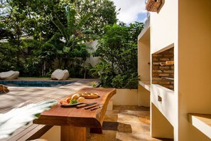 An outdoor dining area with a wooden table, a pool, and lush greenery. - Deluxe Triple Suite at Villa Lux Do Mar (Jijoca de Jericoacoara)