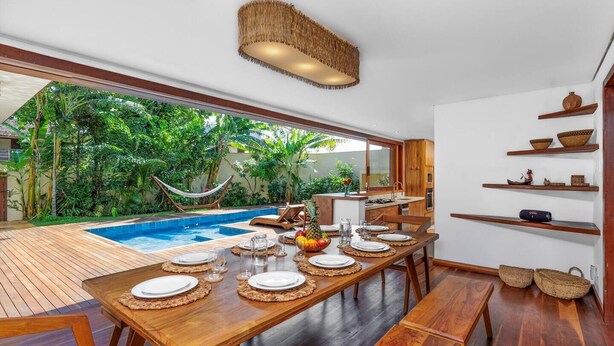 A dining area with a pool view, wooden furniture, and a tropical garden. - Deluxe Triple Suite at Villa Lux Do Mar (Jijoca de Jericoacoara)