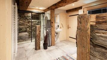 Ein Badezimmer mit Steinwand, Duschkabine aus Glas, Waschbecken und Holzbalken.