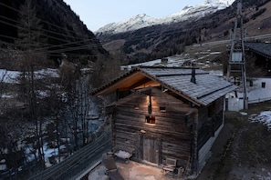 Eine Holzhütte mit Satteldach, ein Steinweg zum Eingang und im Hintergrund eine Flusslandschaft mit Bergen.