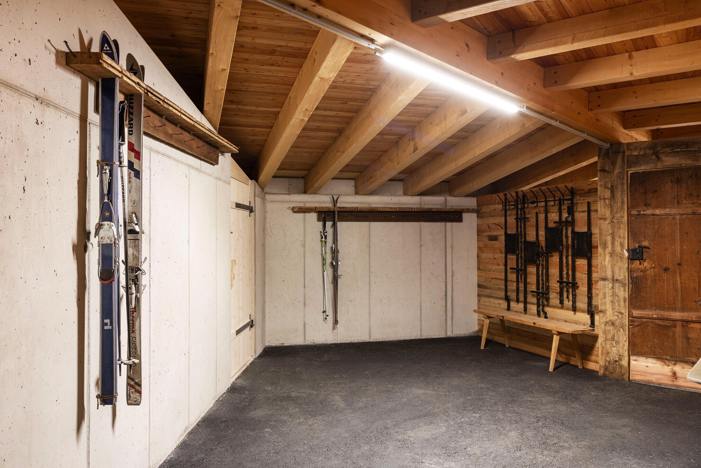 A ski storage room with wooden beams, a slanted ceiling, and skis and ski poles hanging on the walls.