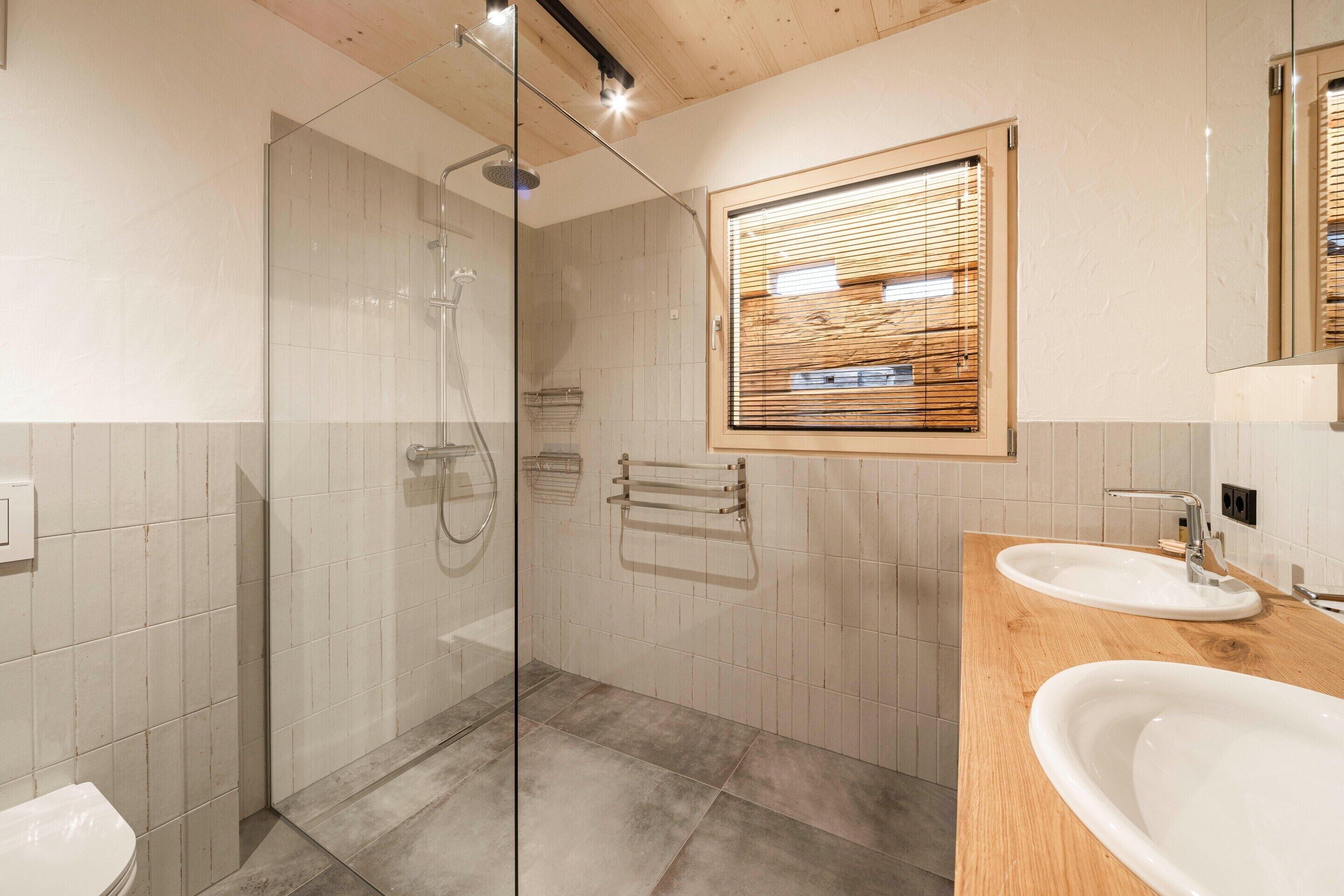 A modern bathroom with a glass-enclosed shower, a wooden vanity with a sink, and a window with blinds.