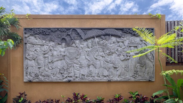 A detailed stone relief sculpture on a wall, surrounded by various plants.