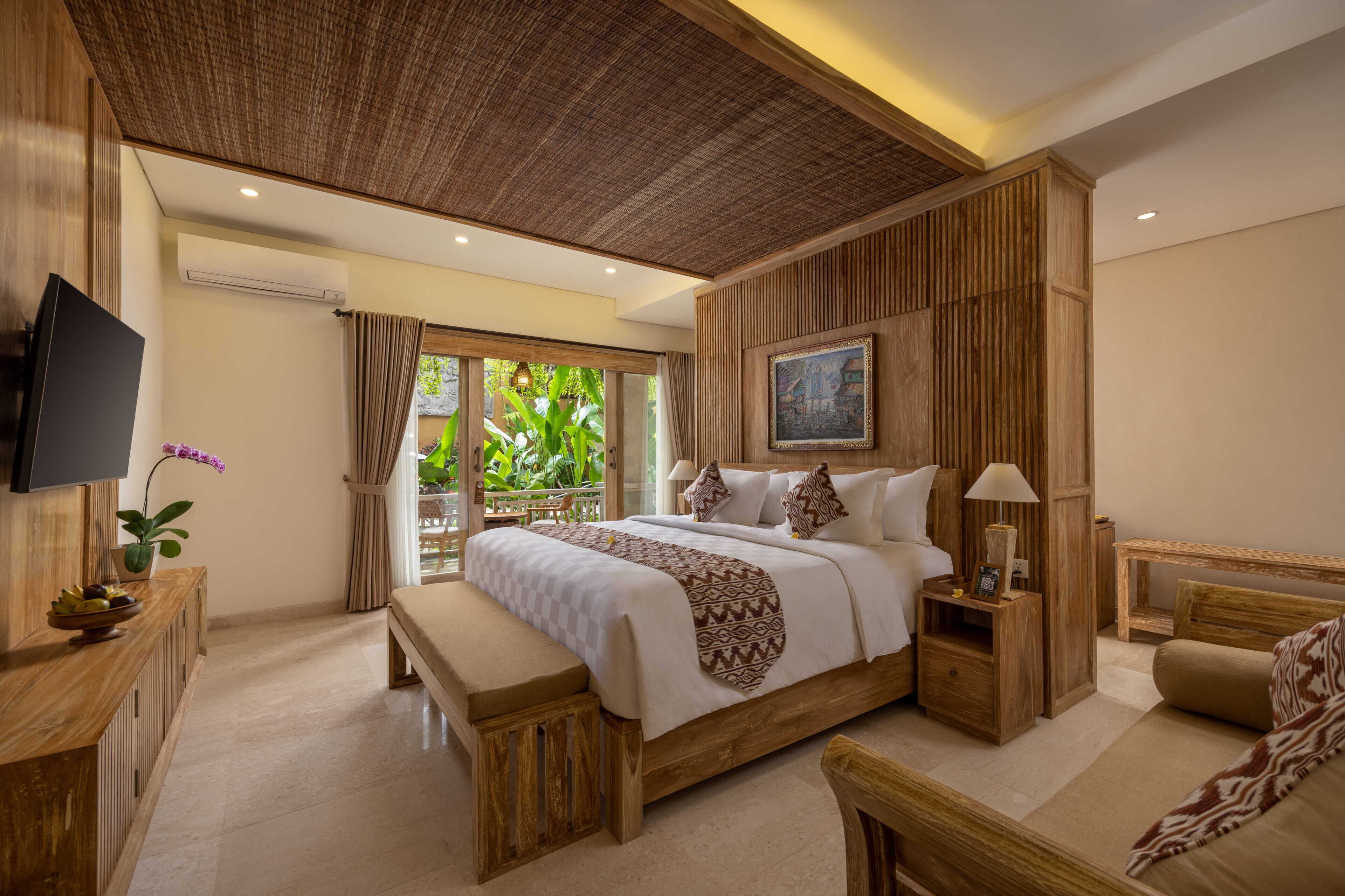 A bedroom with a large bed, a TV, a wooden desk, and a bench.
