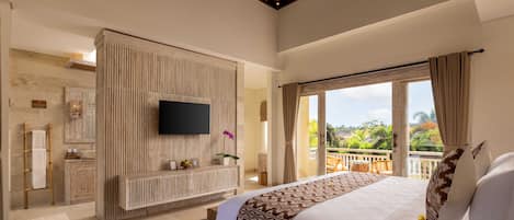 A spacious bedroom with a large bed, a TV mounted on a wooden panel, a balcony with a view of greenery, and a bathroom with a wooden vanity.