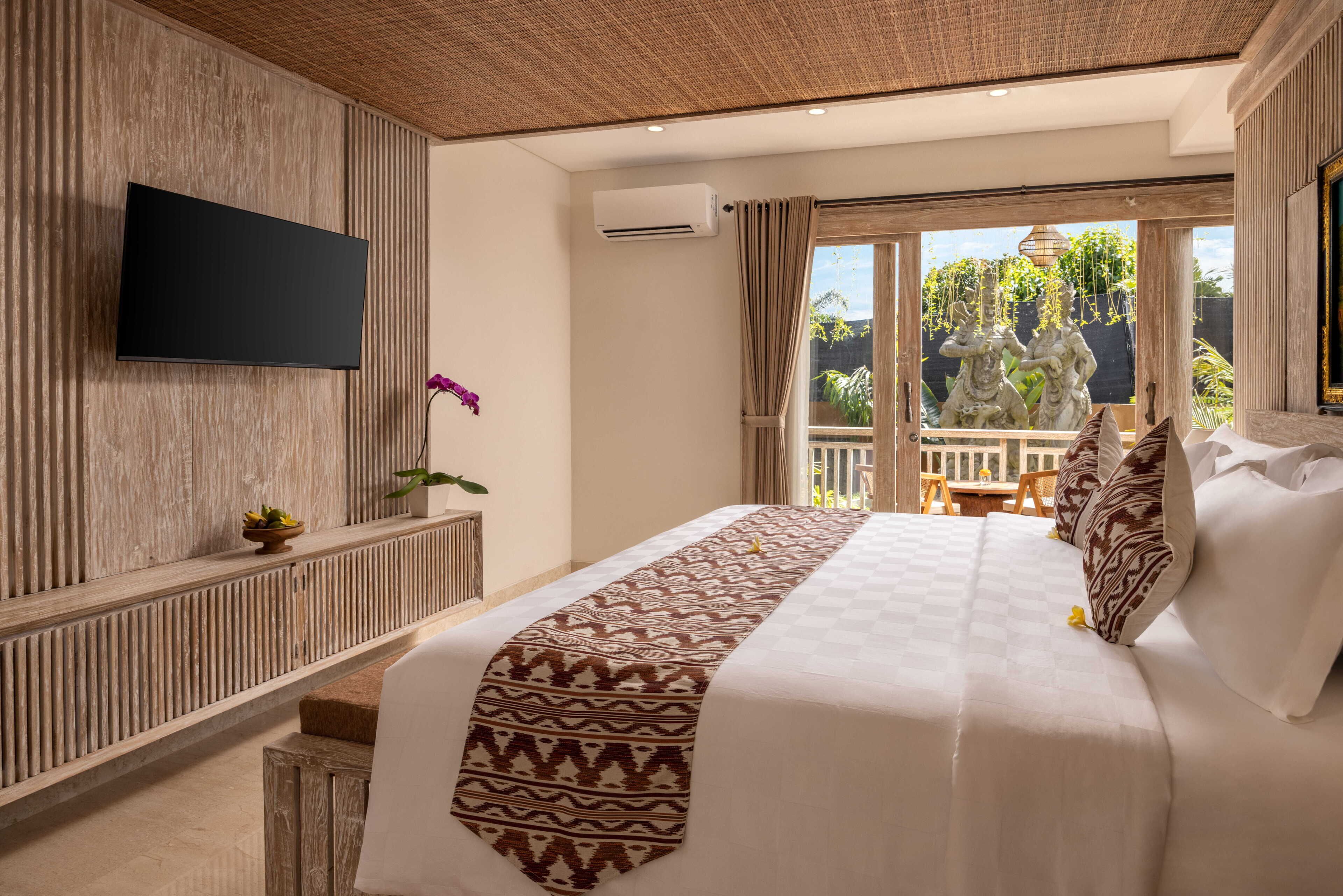 Ein Hotelzimmer mit einem Bett, einem Flachbildfernseher, einer kleinen Topfpflanze und Blick ins Freie.