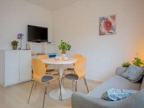 Un salón moderno con un sofá gris, una mesa de comedor con sillas, un televisor de pantalla plana sobre un mueble bajo y un cuadro en la pared.