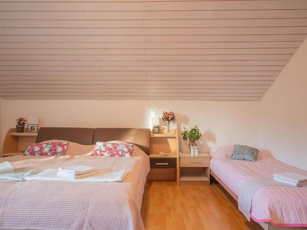 A bedroom with two beds, wooden flooring, a sloped ceiling, bedside tables, and a nightstand with a plant.