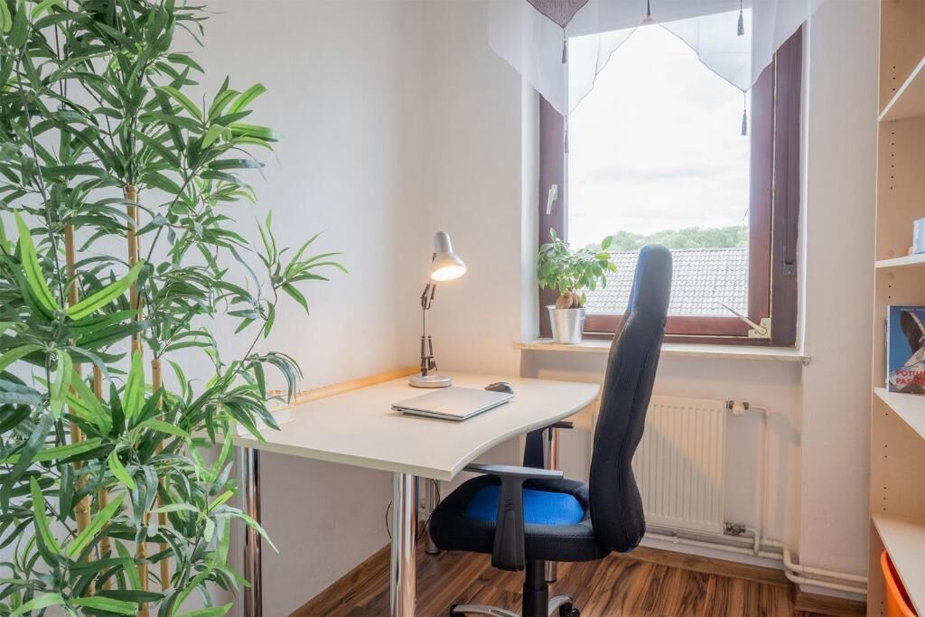A room with a desk, chair, lamp, radiator, window, and a plant.
