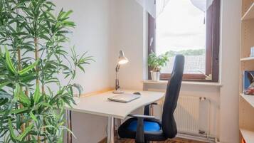 A room with a desk, chair, lamp, radiator, window, and a plant.
