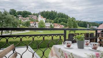 A balcony with a table set for two, overlooking a village with houses and a church.