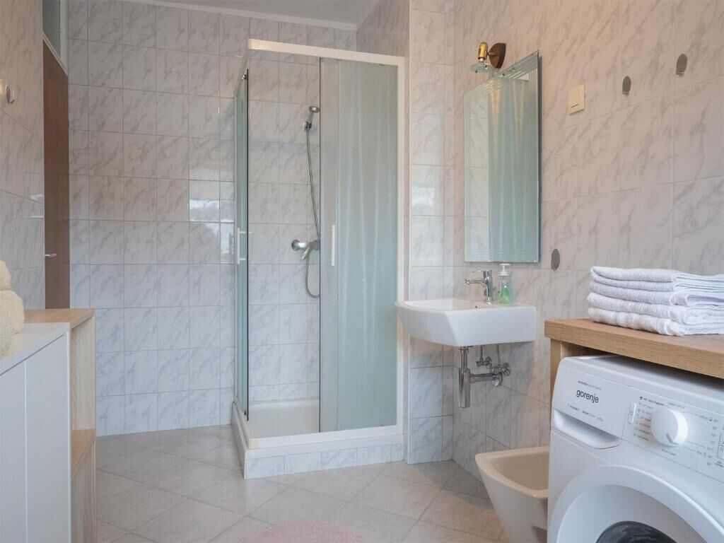 Un baño moderno con ducha envuelta en vidrio, lavamanos y lavadora.