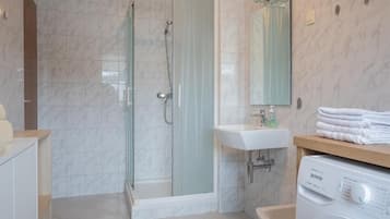 Un baño moderno con ducha envuelta en vidrio, lavamanos y lavadora.