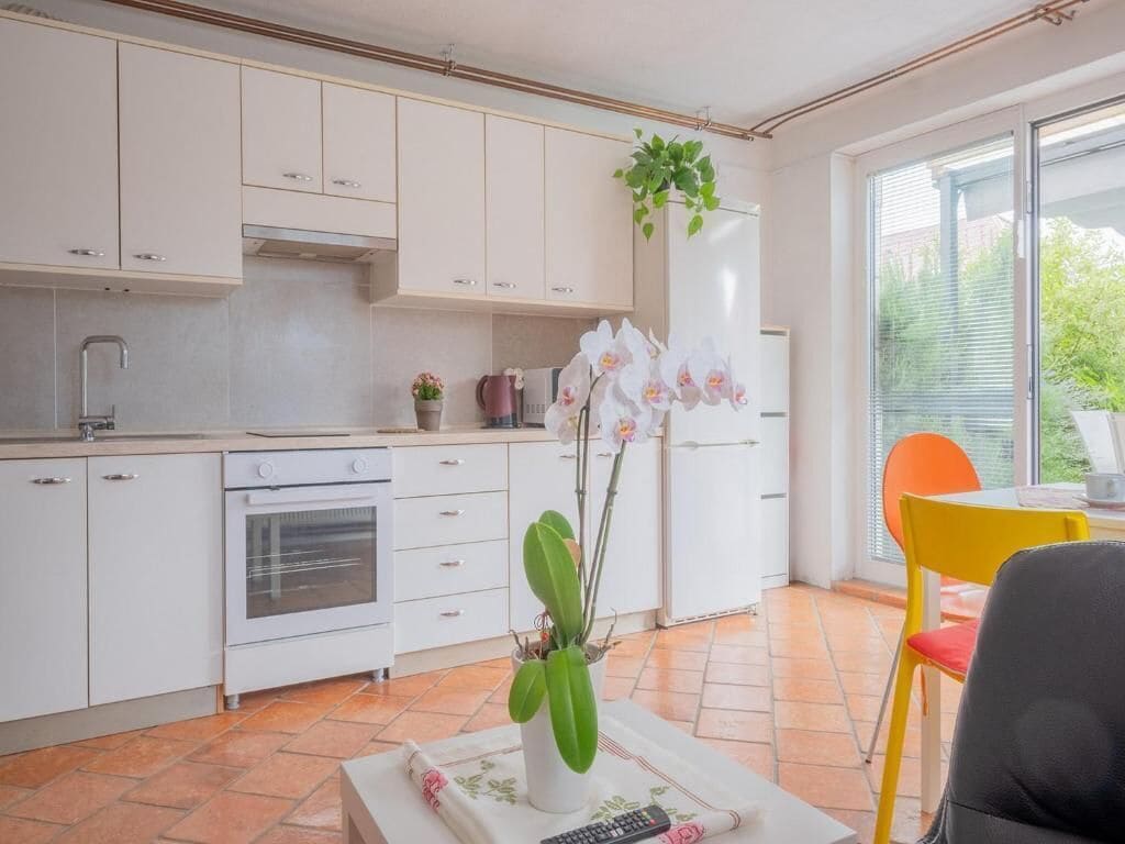 Una cocina moderna con armarios blancos, horno empotrado y comedor con una silla amarilla.