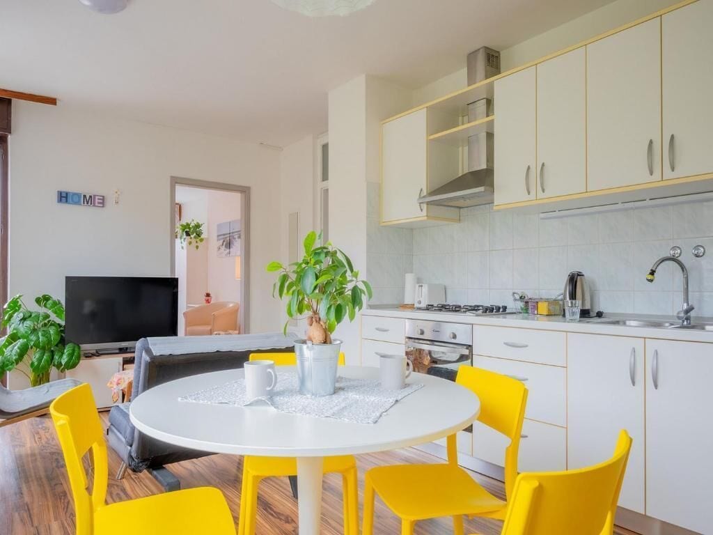 A modern kitchen with white cabinets, a dining table with yellow chairs, and a TV in the living area.