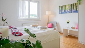 A bedroom with a bed, a desk, a chair, a window, and a painting on the wall.