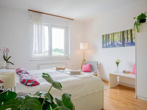 Un dormitorio con cama, escritorio, silla, ventana y un cuadro en la pared.