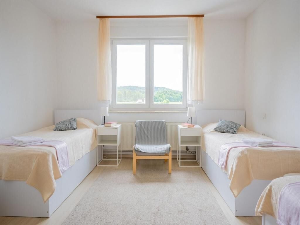 Un dormitorio con dos camas individuales, una silla, una ventana con cortinas y un radiador.