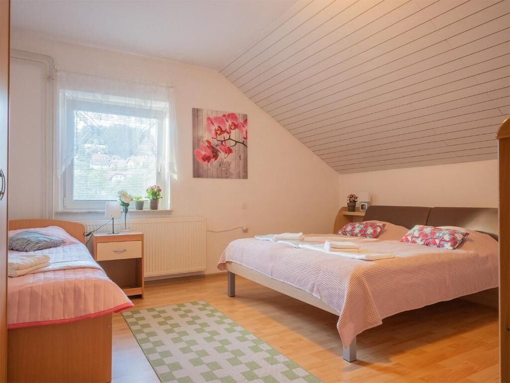 A bedroom with a bed, a bedside table, a window with blinds, a radiator, and a wall-mounted picture.