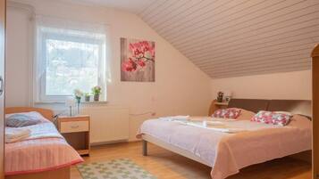 A bedroom with a bed, a bedside table, a window with blinds, a radiator, and a wall-mounted picture.