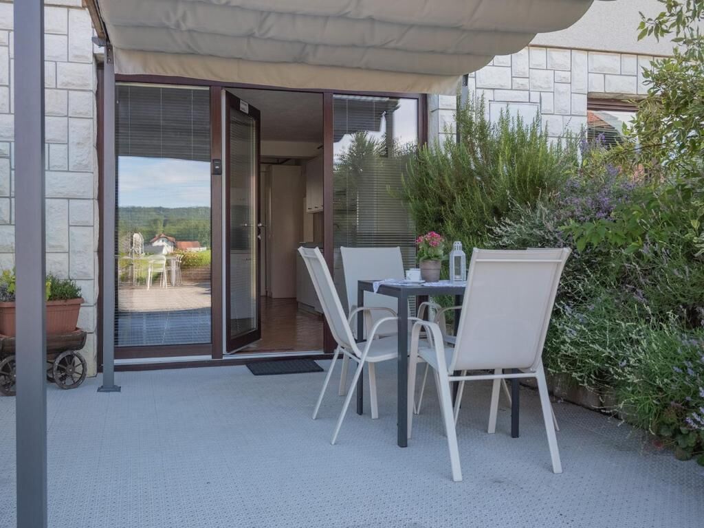 An outdoor patio with a table and chairs, a covered area, and a view of a rural landscape through a glass door.