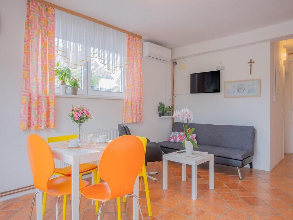 A room with a dining table, chairs, a sofa, a TV, and a cross on the wall.