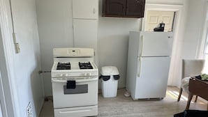 A kitchen with a stove, oven, and refrigerator, a trash bin, and a wooden floor.