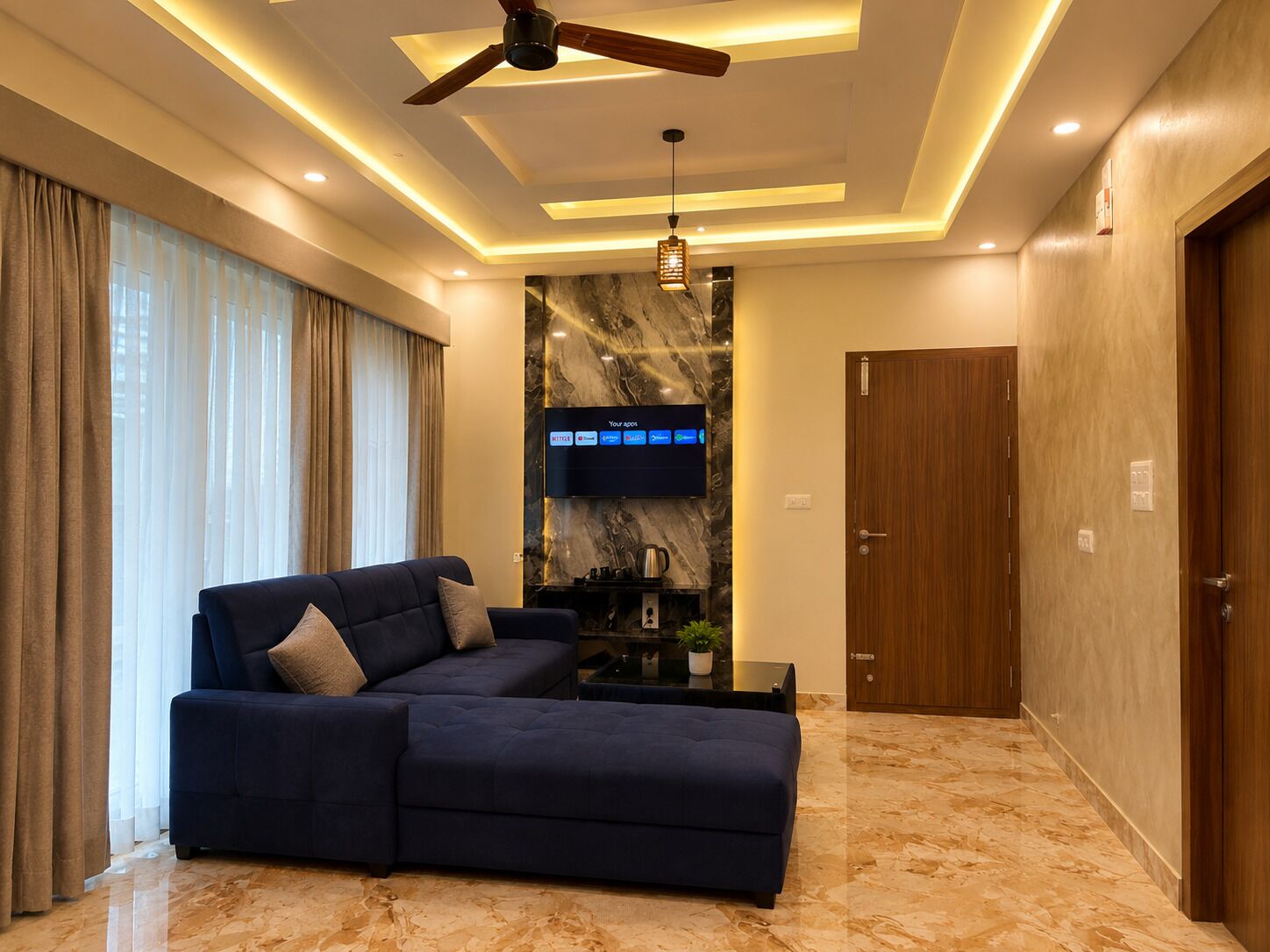 Una sala de estar moderna con un sofá modular, un ventilador de techo, iluminación empotrada, un televisor de pantalla plana y piso de mármol.