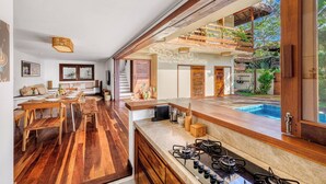 A modern kitchen with a large island, wooden flooring, and a view of a swimming pool. - Deluxe King Suite at Villa Lux Do Mar (Jijoca de Jericoacoara)